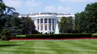 Vista icónica de la Casa Blanca con exuberantes jardines y una fuente central en un día soleado.