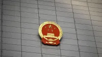 Close-up del emblema nacional chino en una gran fachada de edificio de hormigón, que simboliza la presencia del gobierno.