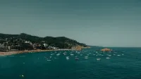 Una pintoresca vista de la costa de Tossa de Mar con barcos y exuberantes paisajes bajo un cielo despejado.