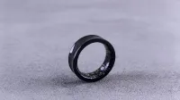 A modern black smart ring with visible circuitry resting on a textured concrete surface.