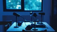 Dimly lit podcast studio with microphones and headphones on a table.