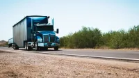 A blue semi truck driving on a rural highway under clear blue skies, showcasing transportation and travel.