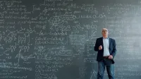 Professor standing in front of a blackboard filled with complex equations and scientific formulas.