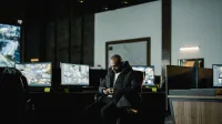 Security officer seated in a dimly lit control room, analyzing multiple surveillance screens.