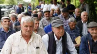 Senior men gathered outdoors, engaging in social interaction under trees.