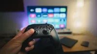 Close-up of a person holding a gaming controller in a cozy living room setup with TV.