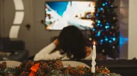 A woman enjoys a cozy evening watching TV by the Christmas tree and candlelight.