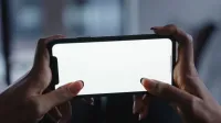 Vista cercana de manos sosteniendo un smartphone con una pantalla blanca en blanco, perfecta para diseños de maquetas.