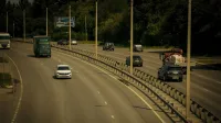 Múltiples vehículos que viajan en una amplia carretera rodeada de árboles en un día soleado.