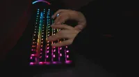 Close-up of hands typing on a colorful RGB backlit mechanical keyboard in a dimly lit environment.