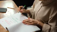 Close-up de una mujer mayor editando un manuscrito en un escritorio con un marcador verde en el interior.