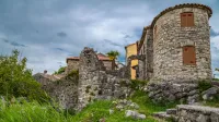 Historic stone buildings amidst vibrant greenery under a cloudy sky.