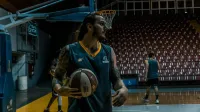 Male basketball players training and practicing in an indoor gym with basketballs and hoops.