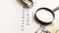 Imagen de cerca de una póliza de seguro con lupa, dinero y coche de juguete.
