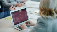 Profesionales de negocios que analizan los datos del mercado de valores en una computadora portátil durante una reunión.