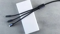 Un elegante banco de energía blanco con un cable multiconector negro colocado sobre una superficie gris texturizada, enfatizando la tecnología moderna.