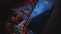 Smartphone Samsung con auriculares rojos y llaves sobre una mesa de madera, en iluminación natural.