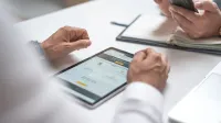 Close-up de profesionales que utilizan una tableta digital y un smartphone durante una reunión.