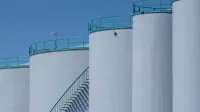 Grandes tanques de almacenamiento industrial con barandillas verdes contra un cielo azul claro.