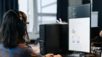 Profesional de TI trabajando en una computadora en un entorno de oficina moderno, enfocado en la codificación y las tareas.