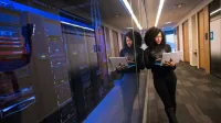 Una mujer que usa una computadora portátil que navega por un centro de datos contemporáneo con servidores reflejados.