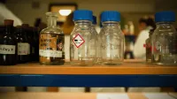 Vista de cerca de botellas de vidrio y contenedores en un estante de laboratorio con símbolos químicos.