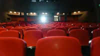 Una vista de un cine vacío con filas de asientos rojos frente a la pantalla iluminada.