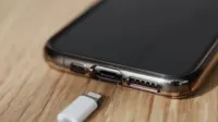 Teléfono móvil moderno en cubierta transparente con cierre de entrada de carga y cable de cargador blanco de teléfono móvil Conector USB en mesa de madera