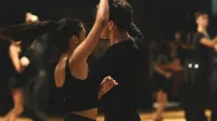 Una pareja que realiza el tango elegantemente dentro de un estudio de baile con espectadores.