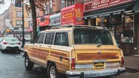 Classic Vintage Wagoneer estacionado en una bulliciosa calle de la ciudad con escaparates y ambiente urbano.