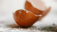 Primer plano de la cáscara de huevo rota colocada en la mesa con harina dispersa en la cocina para cocinar