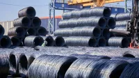 Grandes pilas de bobinas de alambre de acero almacenadas al aire libre en un sitio industrial bajo la luz del día.