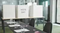 Una mesa de votación preparada con mesas, sillas y cabinas de privacidad en una sala de conferencias.