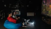 Dos amigos disfrutando de una sesión de videojuegos en una pantalla grande en un ambiente interior acogedor.