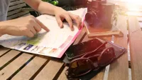 Viajero apuntando al mapa sobre mesa de madera con cámara y accesorios bajo la luz del sol.