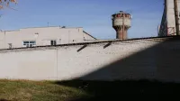 Pared de ladrillo con alambre de púas y una torre de vigilancia bajo un cielo azul claro, lo que sugiere seguridad y protección.