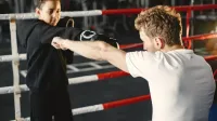 Un joven practica técnicas de boxeo con un entrenador en un gimnasio. Tutoría en deportes.