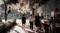 Tres adultos pasean por una pasarela urbana sombreada, iluminada por la luz del sol de verano.