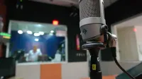Primer plano de un micrófono en un estudio de grabación con un ingeniero de sonido borroso en el fondo.