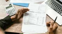 Manos sosteniendo documentos financieros con calculadora y portátil en el escritorio de oficina, escena de análisis de negocios.