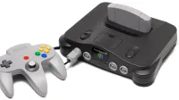Se muestra una consola de videojuegos Nintendo 64 con un controlador gris.