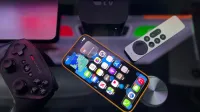 Elegante configuración de entretenimiento en el hogar con un iPhone, Apple TV y controlador de juegos en una superficie oscura.