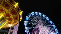 A vibrant Ferris wheel and spinning ride lit up at a night carnival, creating a lively festive atmosphere.