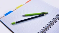 Open spiral notebook with graphing paper, pen, and pencil, ideal for notes or sketches.