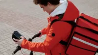 Ciclista de entrega de alimentos comprobando el teléfono inteligente mientras se trabaja. Estilo de vida urbano y tecnología.
