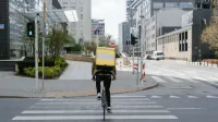 Ciclista con bolsa térmica cruzando la calle en el centro de Varsovia, Polonia.