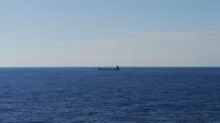 Una escena tranquila de un barco de graneles que cruza un vasto océano abierto bajo un cielo azul despejado.