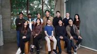 El equipo de Dream Labs, doce personas, de pie y sentado en bloques de madera en un estudio con altas ventanas de fábrica