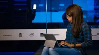 Mujer profesional que trabaja en una computadora portátil en una sala de servidores, mostrando tecnología y trabajo remoto.