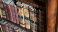 Close-up of vintage leather-bound books on rustic wooden shelves with warm lighting.